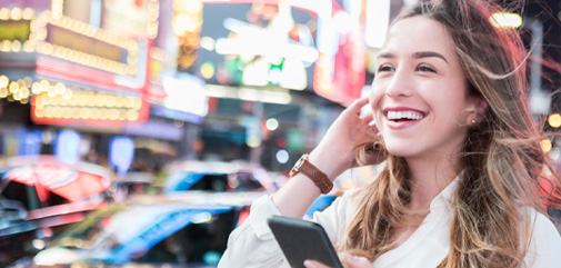 Brunette woman smiling while on her phone outside.