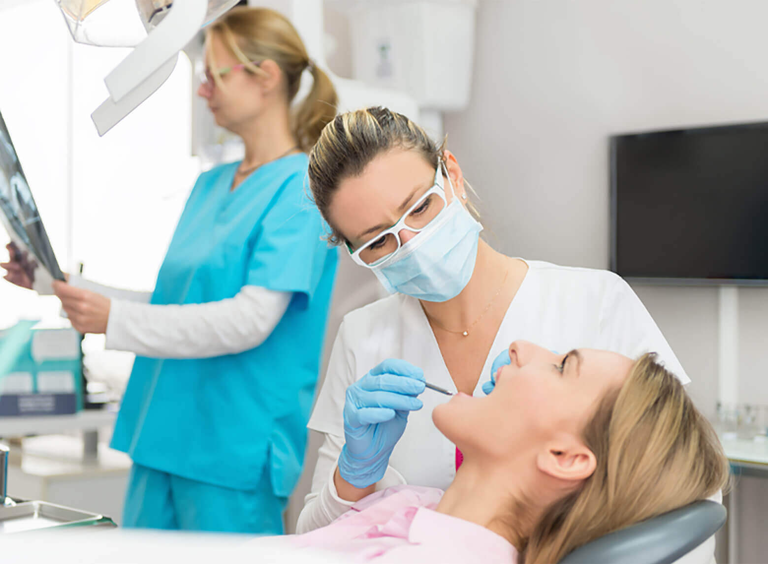 A dentist and her dental assistant are working on patient's teeth inside a dental office.