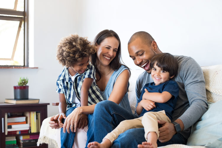 A multiracial family that are patients at Prestige Family Dentistry in Flower Mound, TX smile on a couch