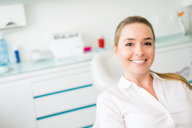 Smiling young woman in dental chair with smooth skin and hair pulled back 