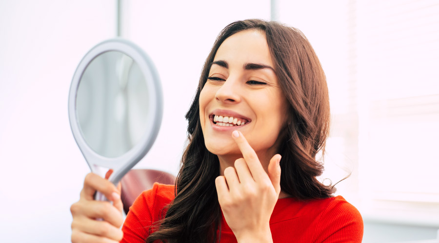 Smiling brunette woman admiring her dental veneers in a hand held mirror