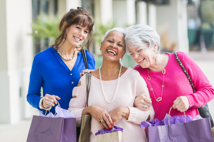 Three laughing mature female friends walking arm in arm with shopping bags