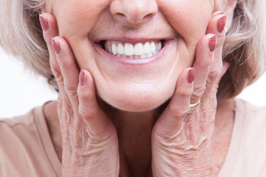 Closeup of a mature woman with her hands on her cheeks and a beautiful smile that benefited from cosmetic dentistry