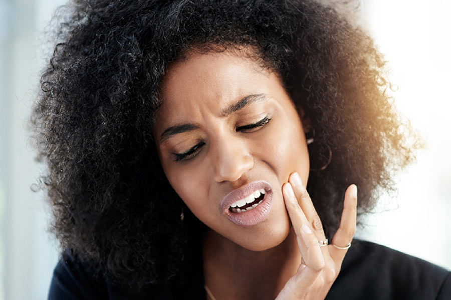 Dark haired, brown skinned woman with a pained look on her face and her hand to her jaw indicating tooth infection