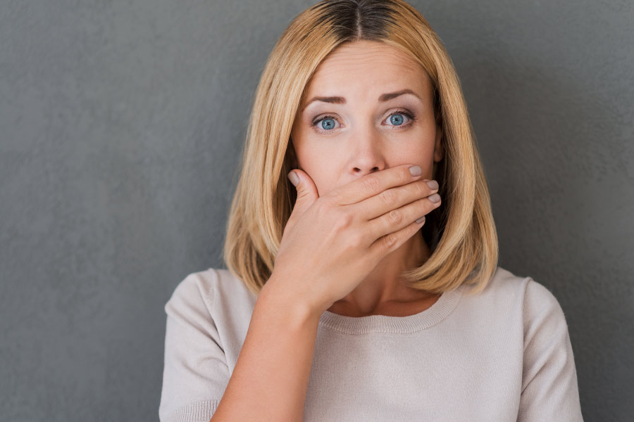 Blonde woman covering her mouth with her hand for fear of bad breath.