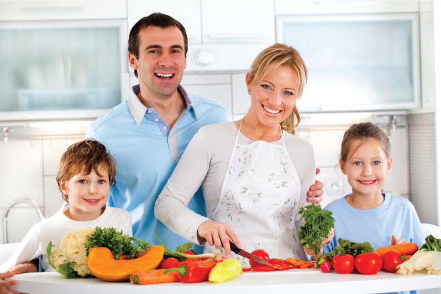 Family of four standing in the kitchen in front of a counter full of healthy foods.