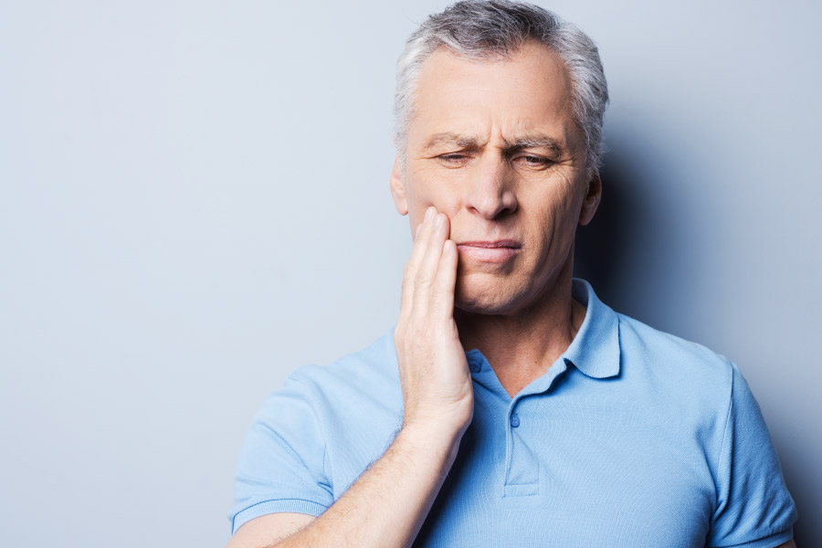 A mature man has a pained look and his hand to his cheek due to tooth pain.