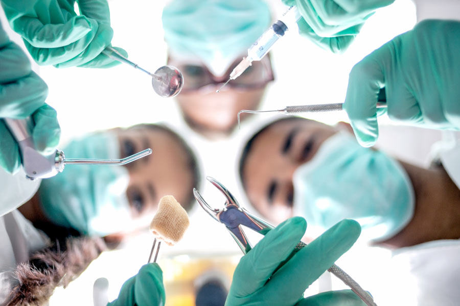 Masked dental professionals with surgical instruments look down on a patient ready for oral surgery.