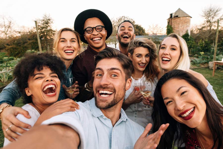A smiling group of multicultural young adults taking a selfie outside.