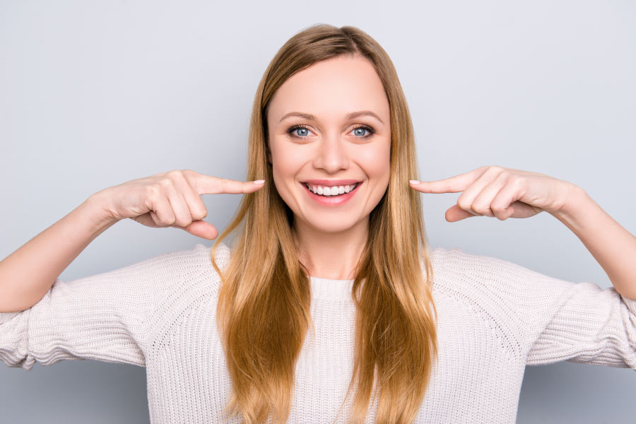 Smiling woman pointing to her recently whitened teeth.