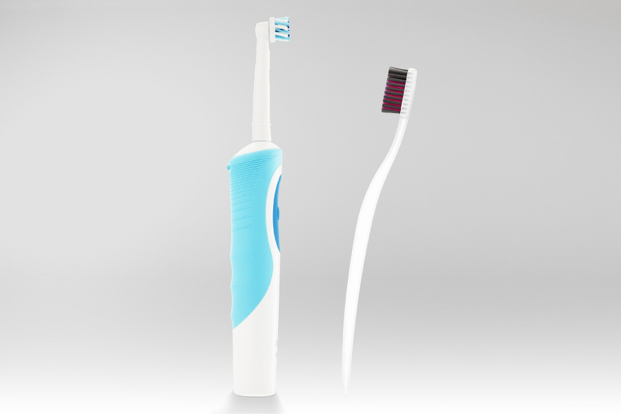 An electric toothbrush standing next to a manual toothbrush.