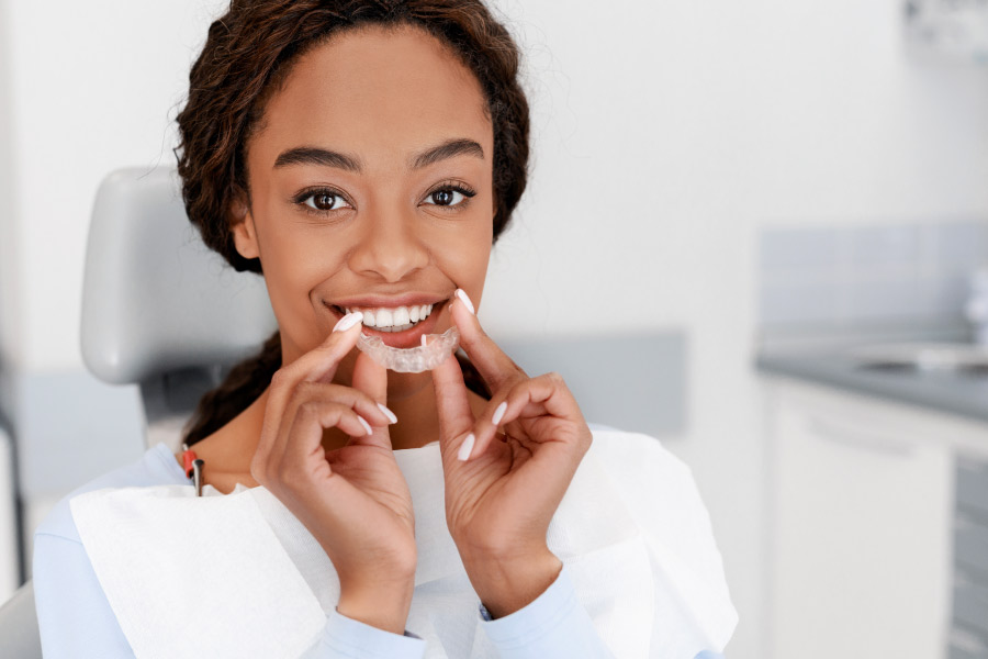 Pretty girl holding up a clear aligner in front of her smile.